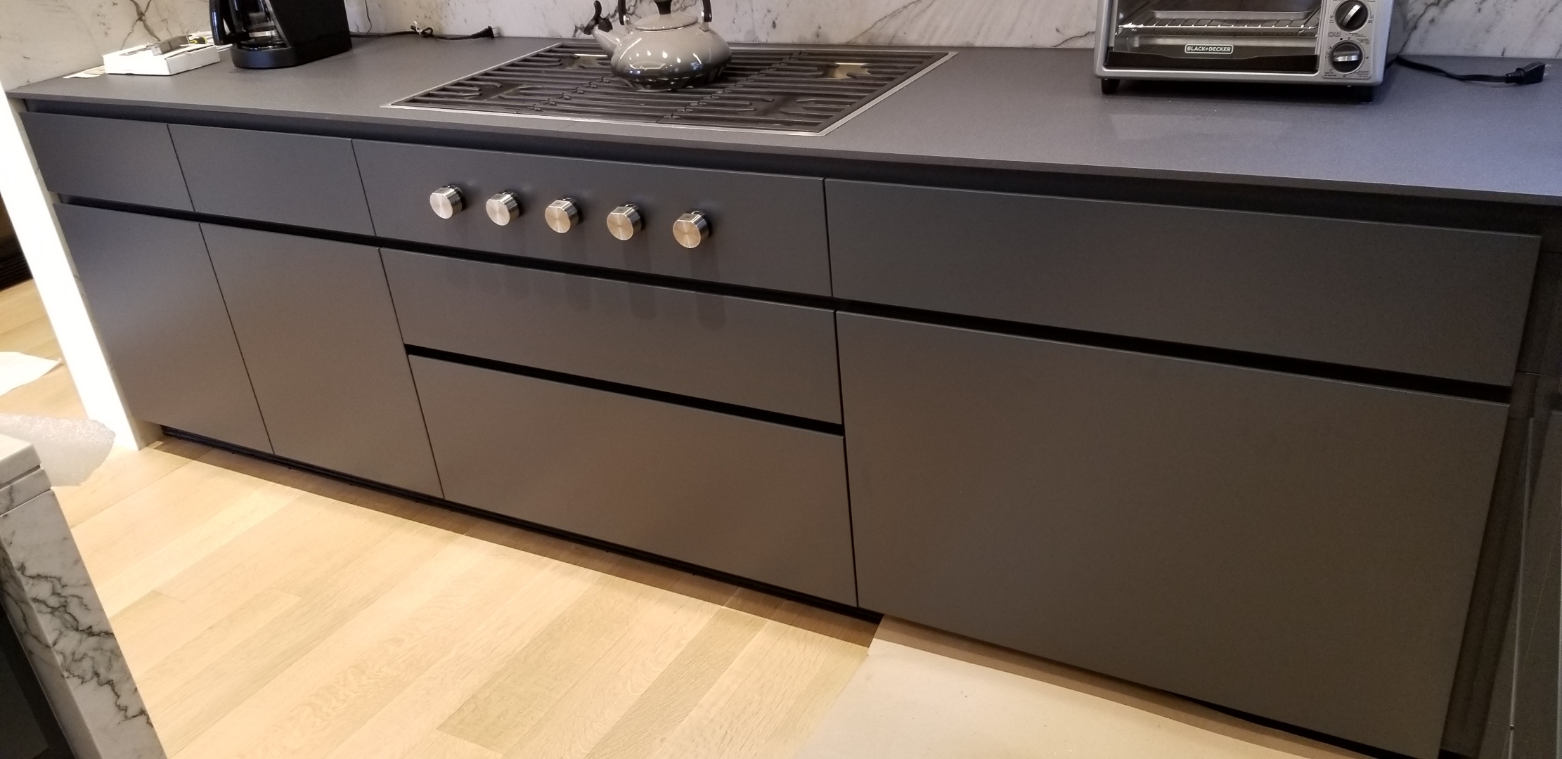 Sleek architectural handleless minimalist kitchen in Oldsmar Florida with smooth solid-color matte charcoal HDF drawer faces, integrated finger-pull horizontal reveal cuts, 3/4 inch maplewood carcasses, and Statuario marble waterfall countertop